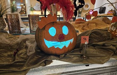 Halloween-Kürbis mit leuchtenden blauen Augen und Mund, trägt eine Krone. Er steht auf einem dekorierten Tisch mit herbstlichen Elementen.