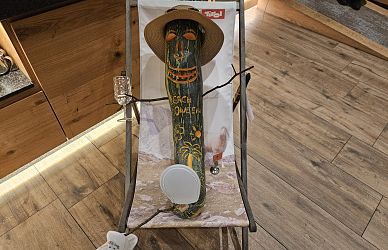 Eine mit lustigen Gesichtern bemalte Gurke sitzt in einem kleinen Liegestuhl. Sie trägt einen Strohhut und hat ein Etikett um den