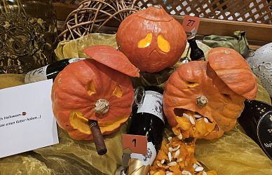 Drei ausgehöhlte Kürbisse mit Schnitzereien stehen auf Flaschen. Ein Kürbis erbricht Kürbiskerne, der andere raucht. Humorvolle Halloween-Dekoration.