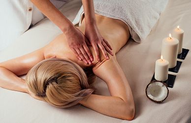 Eine Person erhält eine entspannende Rückenmassage auf einer Liege. Kerzen brennen daneben, und der Raum strahlt eine ruhige, wohltuende Atmosphäre aus.