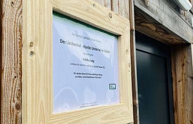 Holztafel an einer Wand mit Text über den Lärchenhof-Martin Unterrainer GmbH. Das Schild informiert über Einparmöglichkeiten, mit einem Holzrahmen um das Dokument befestigt.