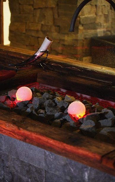 Leuchtende Glaskugeln auf dunklen Steinen, umgeben von Holz, schaffen eine stimmungsvolle und warme Atmosphäre in einem künstlerisch gestalteten Raum.